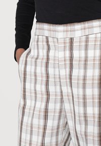 Kárované kalhoty s bílým, béžovým a hnědým vzorem, vyrobené z lehké tkaniny, s bočními kapsami a upraveným střihem.