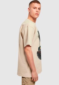 Beige bomulls T-skjorte med avslappet passform, med trykt grafikk av palmer og en bil. Korte ermer og rund hals.