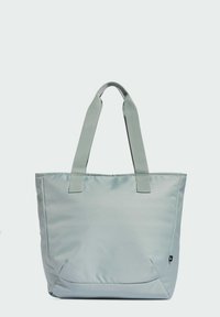 Bolso tote de color gris claro con dos asas de tela, presenta una textura suave y un diseño simple y sin adornos; incluye una etiqueta de logotipo en el exterior.