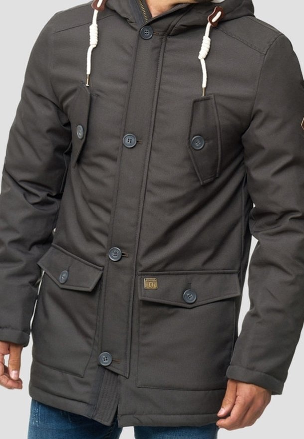 Manteau d’hiver noir à capuche avec fermetures à boutons, deux poches poitrine à boutons et deux grandes poches avant à rabat, porté par une personne avec les mains visibles.