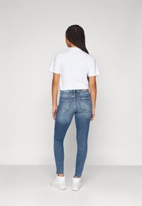 Blå denim skinny jeans med en mid-rise passform, blekningar och två bakfickor, som bärs med en vit t-shirt med kort ärm och vita sneakers.
