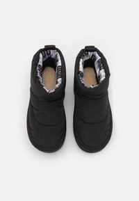 Zapatillas aislantes negras con un interior suave y mullido y un diseño acolchado; cuentan con un forro de patrón en blanco y negro y una puntera redondeada.