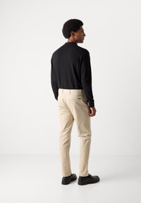 Black long-sleeve shirt paired with beige trousers. The trousers feature back pockets, and the outfit is complemented by black shoes.