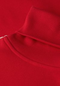 Camisa polo de algodón roja con un cuello acanalado y textura suave, que presenta un diseño curvado y sutiles detalles de costura.