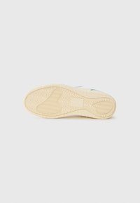 Semelle de chaussure en caoutchouc ivoire avec un motif de traction en zigzag, présentant des zones de texture surélevée et lisses ; design minimaliste sans marque visible.