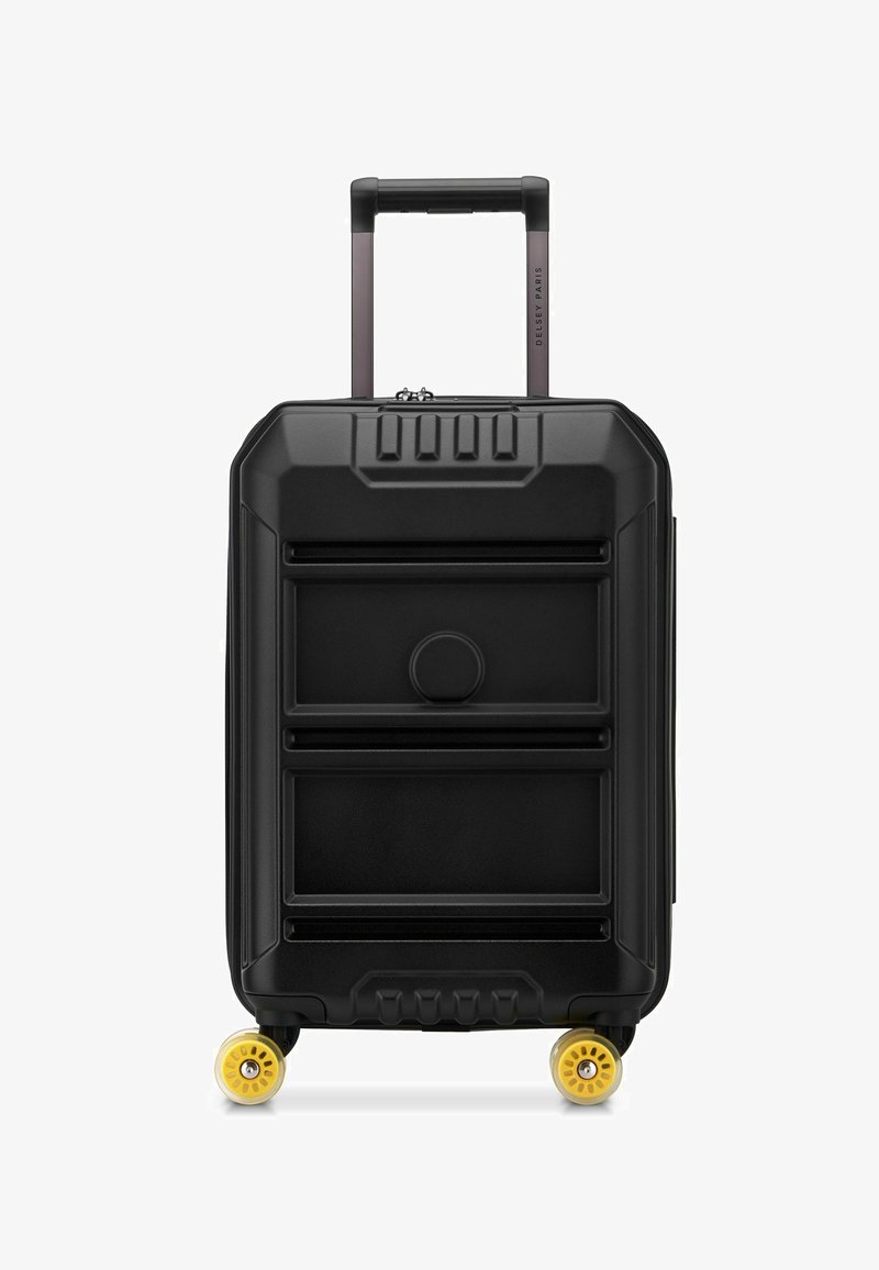 Valise rigide noire avec un devant texturé, poignée rétractable et quatre roulettes jaunes pivotantes, se tenant debout sur un fond blanc.