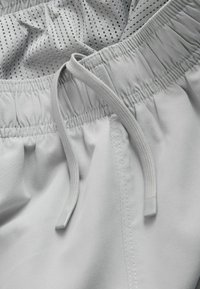 Gros plan sur la ceinture élastique gris clair avec cordon de serrage sur un short, montrant les détails du tissu lisse et perforé.