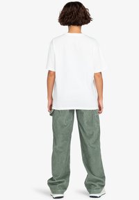 T-shirt en coton blanc avec une coupe décontractée, associé à un pantalon large en velours côtelé vert avec des rayures verticales et des poches latérales.
