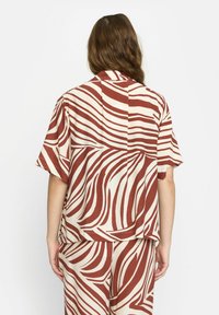 Korte mouw shirt in beige met bruine golfpatronen. Ontspannen fit, lichtgewicht materiaal en zichtbare naden. Geschikt voor casual draag.