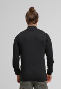 Suéter negro de punto con cuello alto, diseño ajustado, puños y dobladillo acanalados, que muestra una textura suave y un minimalismo en los detalles.
