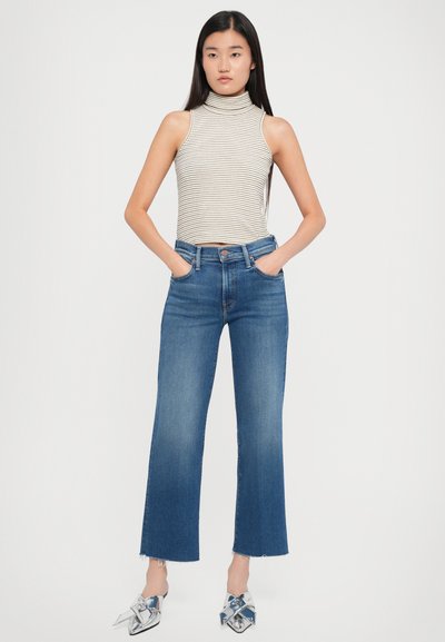 Top a collozzo a righe senza maniche, jeans a campana blu a vita alta con orlo sfrangiato, abbinati a mule argentati.