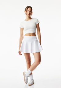 Camiseta blanca corta y falda blanca acampanada. La modelo lleva zapatillas deportivas grises y calcetines blancos. Tela suave con detalles de diseño mínimos.