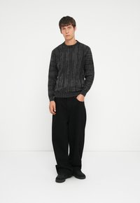 Black textured sweater with ribbed cuffs and hem, featuring a wavy pattern, paired with loose black trousers and black sneakers.