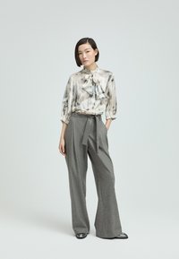 Helle Bluse mit einer Schleifenkragen, kombiniert mit hoch taillierten, grauen, gestreiften weiten Hosen und schwarzen Schuhen.