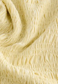 Világossárga szövet, melynek felülete texturált és redőzött hatású. A felület sima, kiemelkedő elasztikus redőzésekkel, egységes mintázatban.