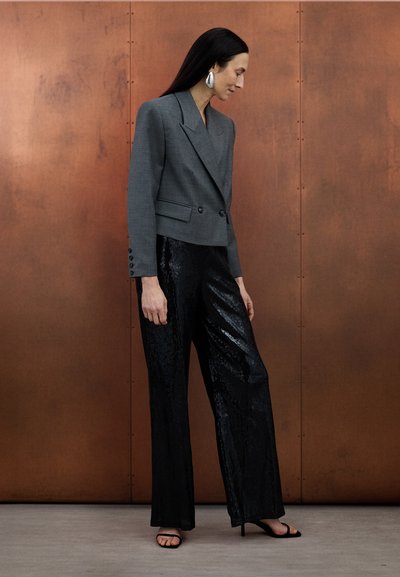 Γκρι σακάκι διπλής σειράς με κουμπιά, συνδυασμένο με μαύρο παντελόνι φαρδύ με παγιέτες. Το σύνολο περιλαμβάνει απλά μαύρα σανδάλια και τολμηρά σκουλαρίκια-δηλώσεις.