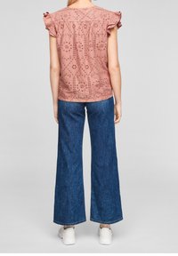 Blusa di cotone rosa con motivi a occhio, maniche corte a volant; abbinata a pantaloni in denim a gamba larga blu. Sneakers bianche completano il look.