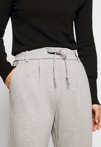Grijze casual broek met een trekkoord in de taille, zijzakken en een relaxte pasvorm; gecombineerd met een zwart langemouwen shirt. Zachte stofstructuur.