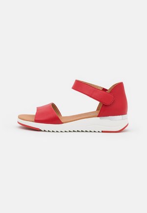Rød sandal med åben tå og justerbar ankelrem, polstret tan indersål, hvid tyk sål med sølv accent og rødt slidmønster.