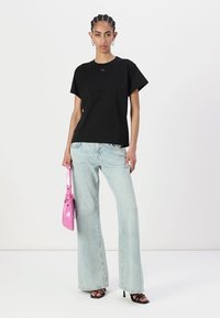Black short-sleeve t-shirt, relaxed fit, paired with light blue wide-leg jeans. Accessories include a shiny pink handbag and black heeled sandals.