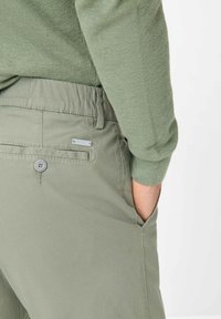Light green pants with a textured finish, elastic waistband, front and back pockets, and a small metallic accent near the back pocket.