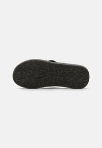 Semelle extérieure en caoutchouc noir avec un motif texturé, présentant diverses formes géométriques pour une meilleure adhérence. Côtés renforcés avec un profil plat.