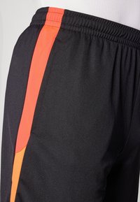 Black athletic shorts featuring a red and orange accent stripe, elastic waistband, and soft polyester fabric texture.