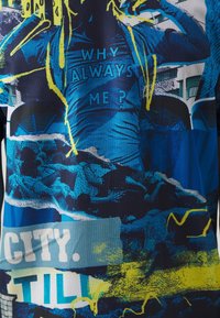 Grafická tričko s modrým a černým potiskem s žlutými akcenty, na kterém je nápis "PROČ VŽDY JÁ?" a abstraktní obrazce.