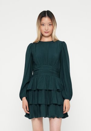 Türkis Kleid pikade pikkade, puhviga varrukatega, pleeditud kehaga ja kihiliste lõhikute seelikutega. Valmistatud kergest kangast, millel on pehme tekstuur.