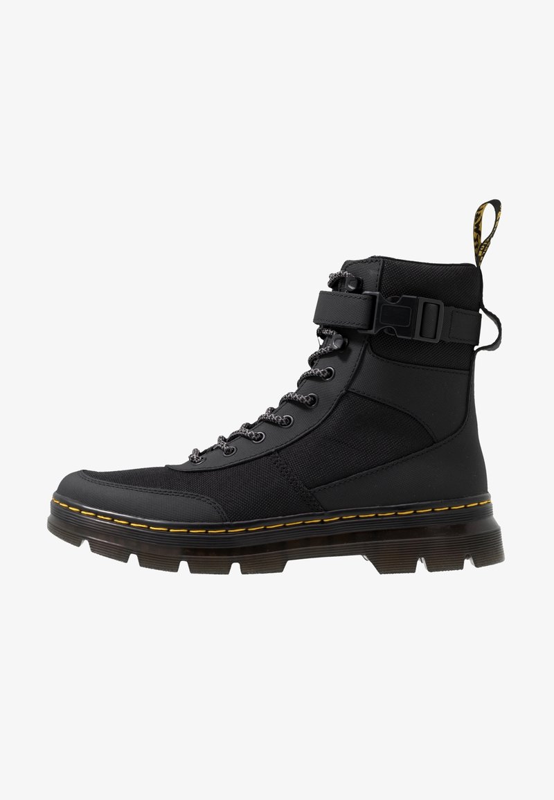 Botte montante noire avec semelle épaisse, œillets métalliques, lacets, bride à boucle et surpiqûres jaunes le long du bord de la semelle.