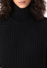 Black ribbed turtleneck sweater with textured, form-fitting design; features high neck and long sleeves, showcasing a smooth, cozy knit.