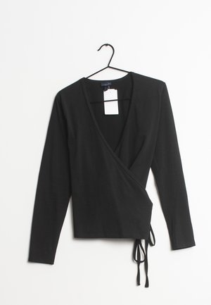 Zwart lange mouwen wikkel top met V-hals en strikdetail aan de zijkant, hangend aan een zwarte hanger tegen een witte achtergrond.