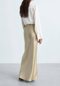 Falda de satén beige combinada con una blusa de seda blanca, que presenta mangas largas y un corte holgado. La falda cae suavemente hasta el suelo.