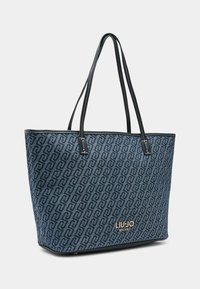 Borsa tote in tela blu con un motivo geometrico. Presenta manici in pelle, dettaglio logo dorato e cuciture a contrasto lungo i bordi.
