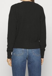 Sort strikket sweater med ribbet tekstur, rund hals og faldende skuldre, kombineret med lyseblå jeans.