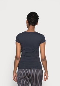 Camiseta ajustada de color marino con mangas cortas, textura suave y escote redondeado. Combinada con pantalones de rayas, mostrando una vista trasera suave.