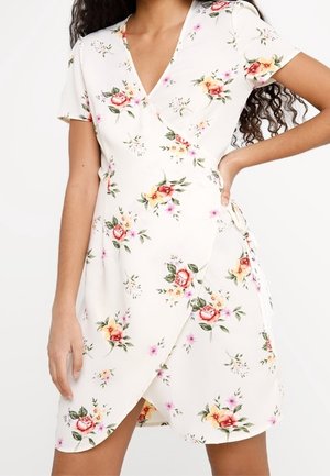 Blumenkleid in Creme, mit kurzen Ärmeln, tiefem V-Ausschnitt und seitlichem Band. Der Stoff hat eine weiche Textur mit rosa und gelben Blumenmustern.