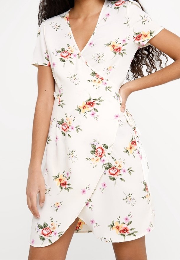 Květinové zavinovací šaty v krémové barvě, s krátkými rukávy, hlubokým výstřihem do V a bočním zavazováním. Látka má jemnou strukturu a je pokryta vzory růžových a žlutých květin.