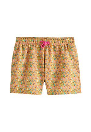 Mężczyzna w okularach przeciwsłonecznych, białej koszuli z krótkim rękawem i wzorzystych kąpielówkach spaceruje boso obok basenu w słoneczny dzień.