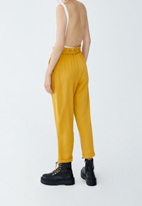 Gula, hög midja byxor med en samlad midja, smal passform och uppvikta manschetter, i kombination med svarta snörkängor. Slät tygtextur.