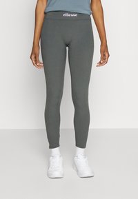 Legging gris avec un design ajusté, fabriqué en tissu extensible, présentant un logo violet visible sur la ceinture et associé à des baskets blanches.
