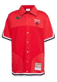 Maillot rouge à manches courtes avec fermeture à boutons, présentant une broderie "CHICAGO BULLS", un logo de taureau, et des accents noirs et blancs à l'ourlet.