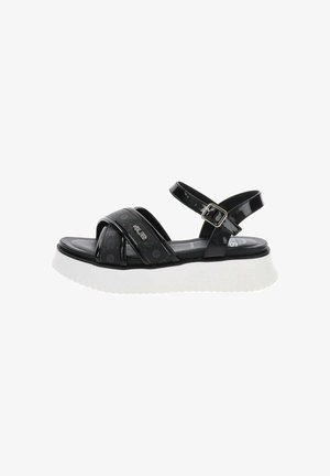 Sandalia negra con punta abierta, tira ajustable en el tobillo, tiras delanteras cruzadas con logotipos y suela blanca gruesa para uso informal.