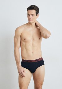 Schwarze Baumwollslips mit einem roten Nike-Logo-Bund; enganliegendes Design, glatte Textur und minimale Nähte für Komfort.