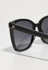 Lunettes de soleil noires surdimensionnées avec des verres teintés foncés, des montures épaisses et un petit logo multicolore sur la tige. Fini en plastique lisse.