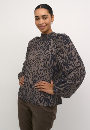 Brown leopard print blouse with a smocked high neck, voluminous long sleeves, and gathered cuffs, paired with dark brown pants.