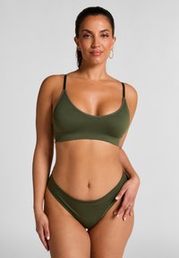 Bralette vert olive avec des fines bretelles noires, présentant un col rond et un design sans coutures. Le look est complété par un bas de bikini taille haute assorti.