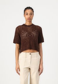 Top corto a maniche corte in maglia marrone con motivo traforato, scollo ampio e vestibilità cropped, abbinato a pantaloni beige chiaro a vita alta.