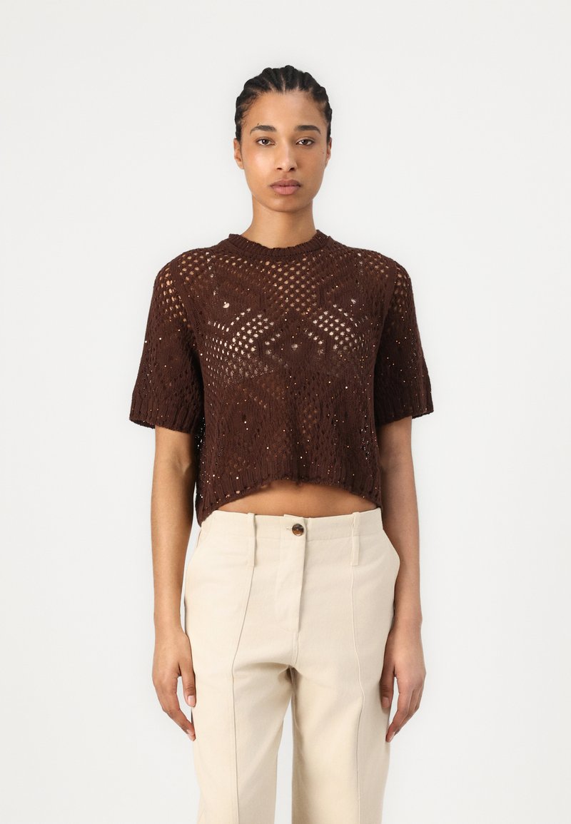 Top corto a maniche corte in maglia marrone con motivo traforato, scollo ampio e vestibilità cropped, abbinato a pantaloni beige chiaro a vita alta.
