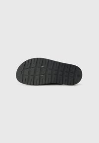 Semelle de chaussure en caoutchouc noire avec un motif de bande de roulement texturé, un orteil arrondi et un profil plat. Comprend des rainures de flexion pour une meilleure adhérence et flexibilité.